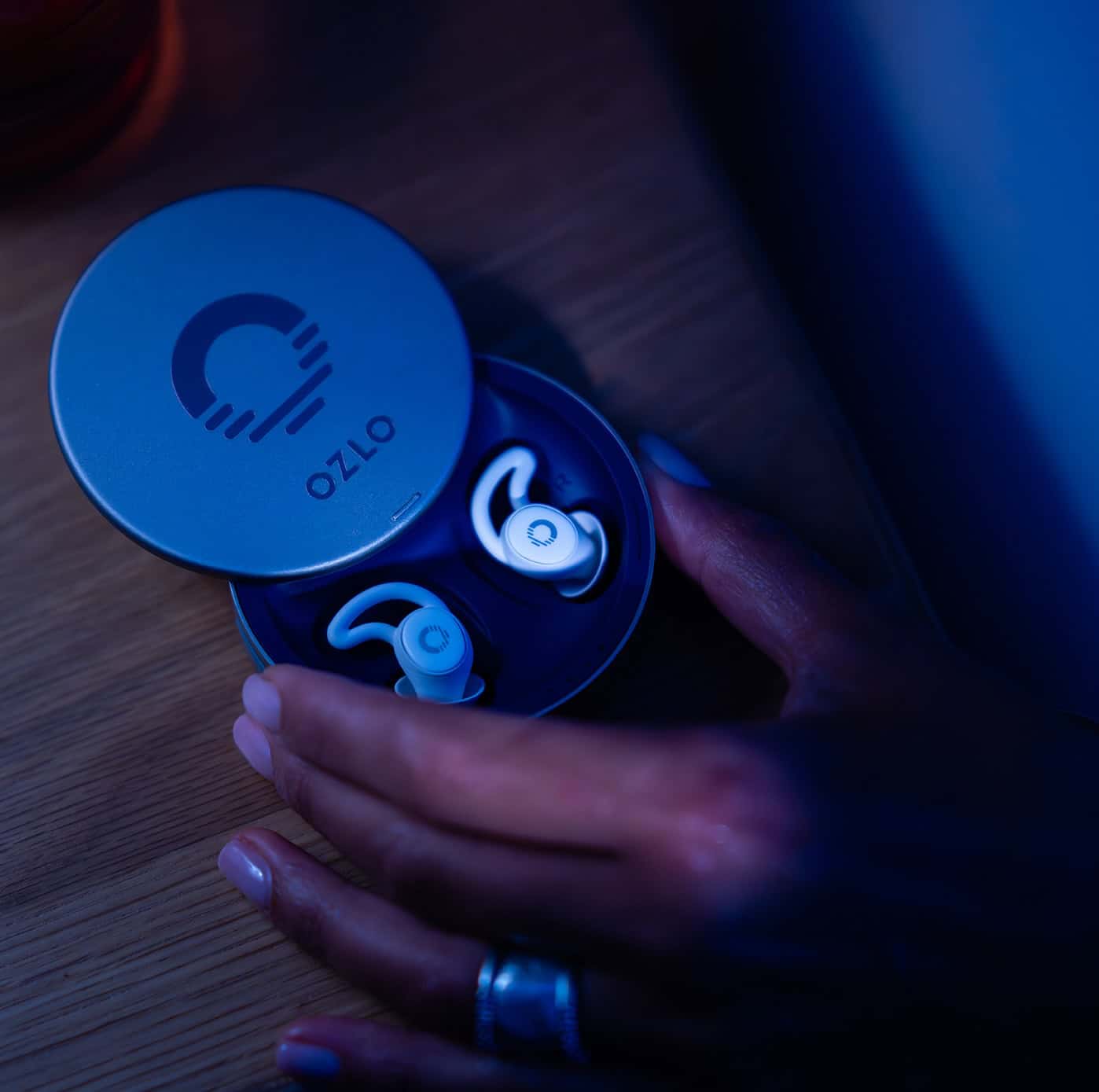 White wireless earbuds resting in an open circular charging case on a dark wooden bedside table.